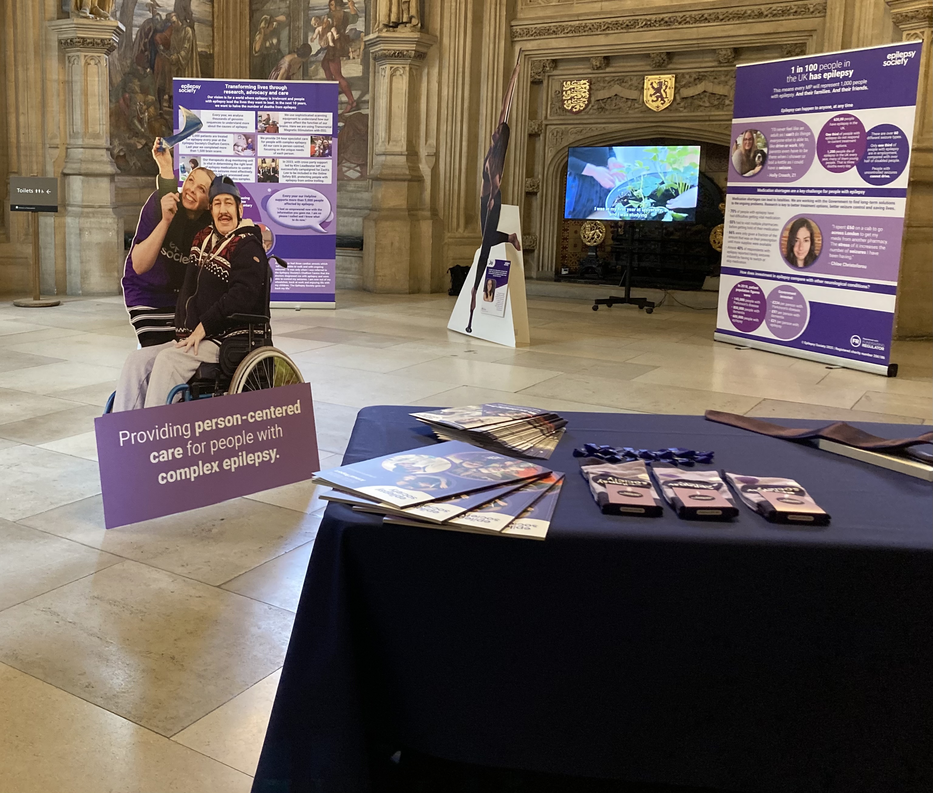 Image shows large pull up banners which show the impact of epilepsy and the work we are doing to address it. Also, cut outs of some of our beneficiaries including one young woman who is now able to learn to pole dance
