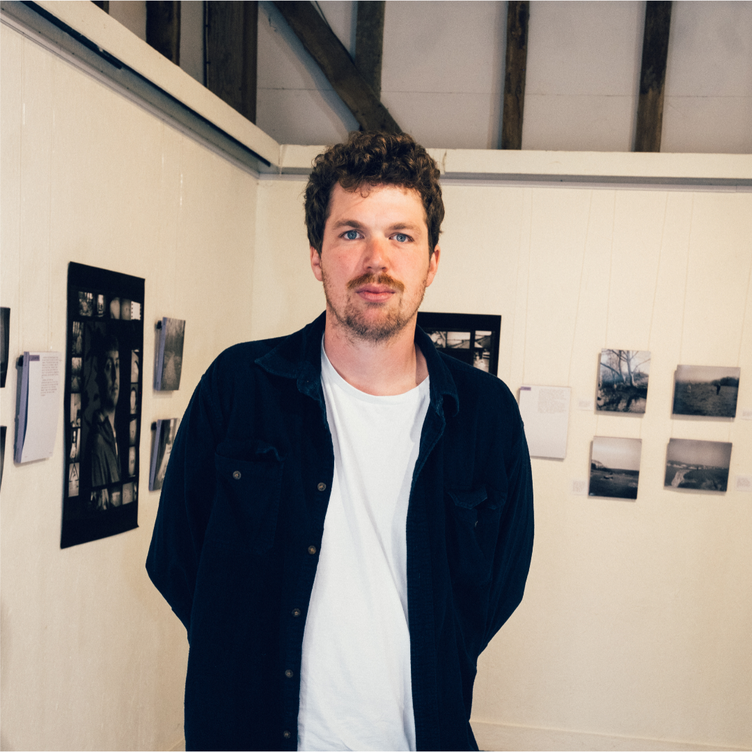 Image of man with curly hair and a beard standing in front of a display of photographs