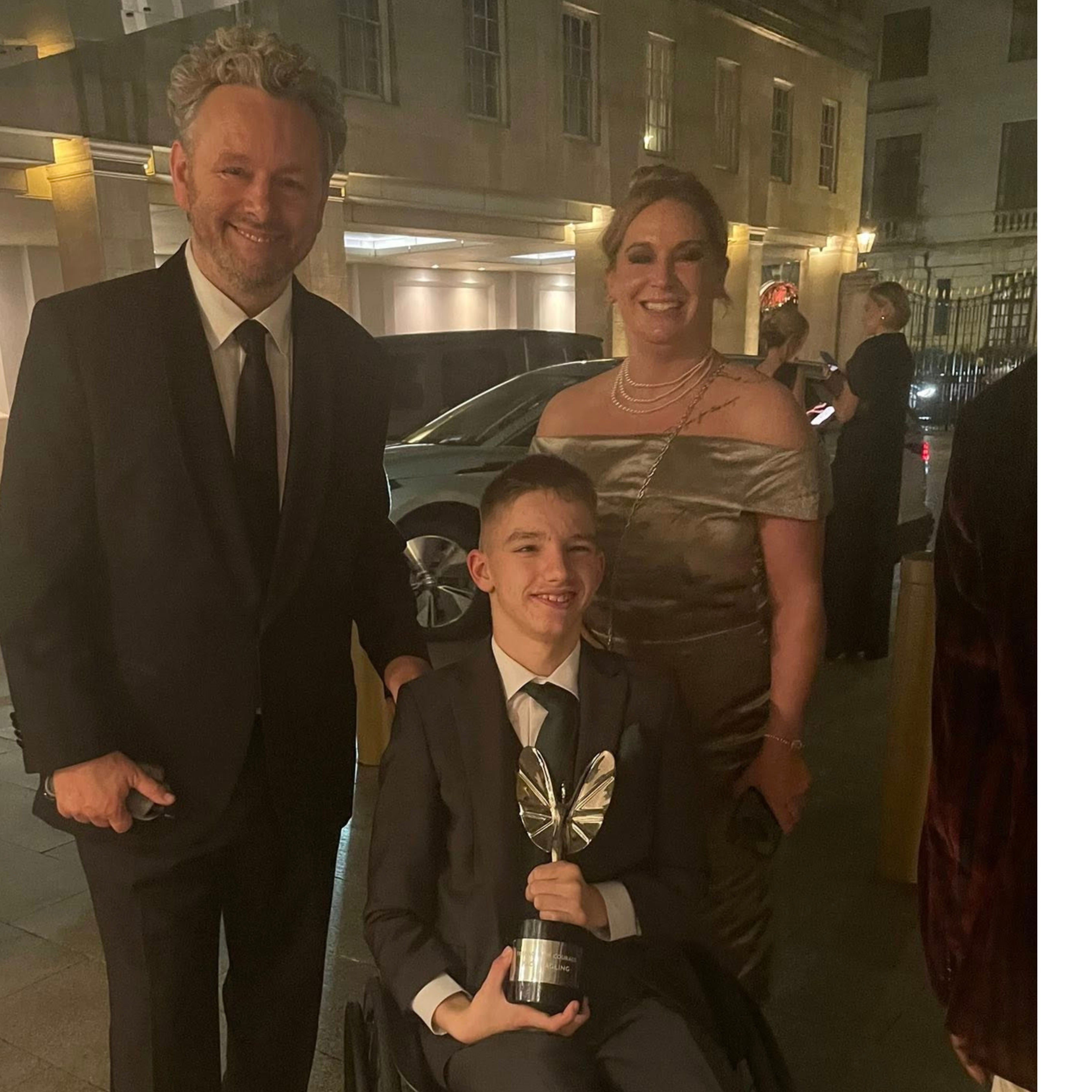Actor Michael Sheen with Zach Eagling, young man in wheelchair holding Pride of Britain award with his Mum standing behind