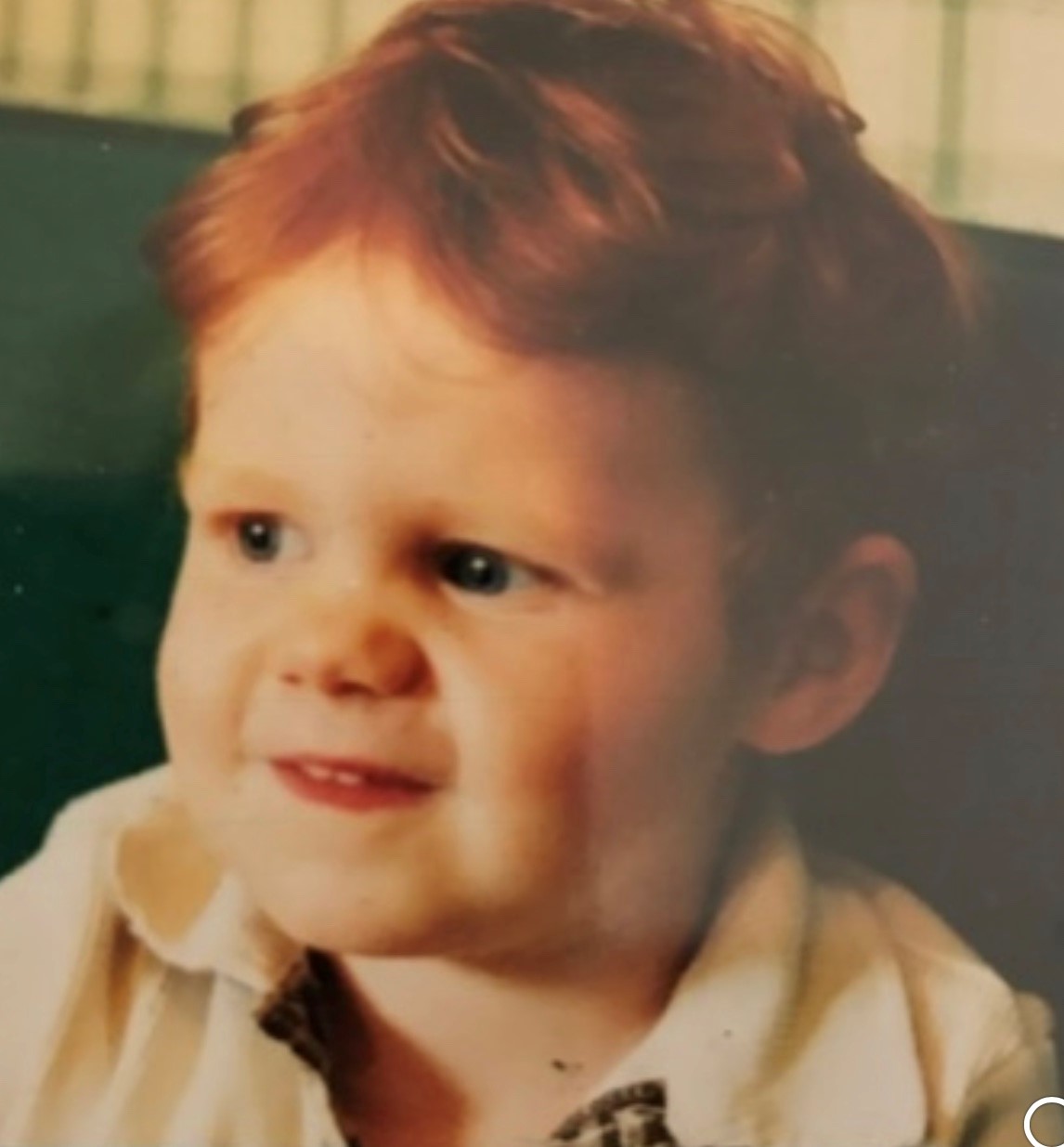 Muir as a toddler with bright red hair and a cheeky grin.