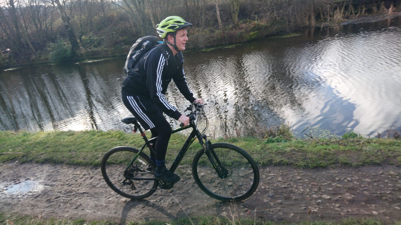 Cyclist Elliott Horan is cycling beside a waterway, in full cycling gear.