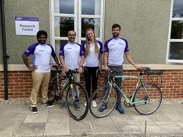 Four members of our Genomics Research Team are standing with their bikes outside the research centre. They are wearing purple and white Epilepsy Society tops