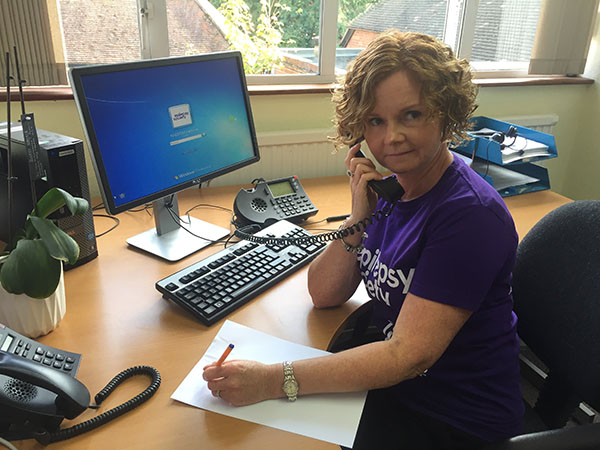 Woman in purple t-shirt, at a desk and on the phone