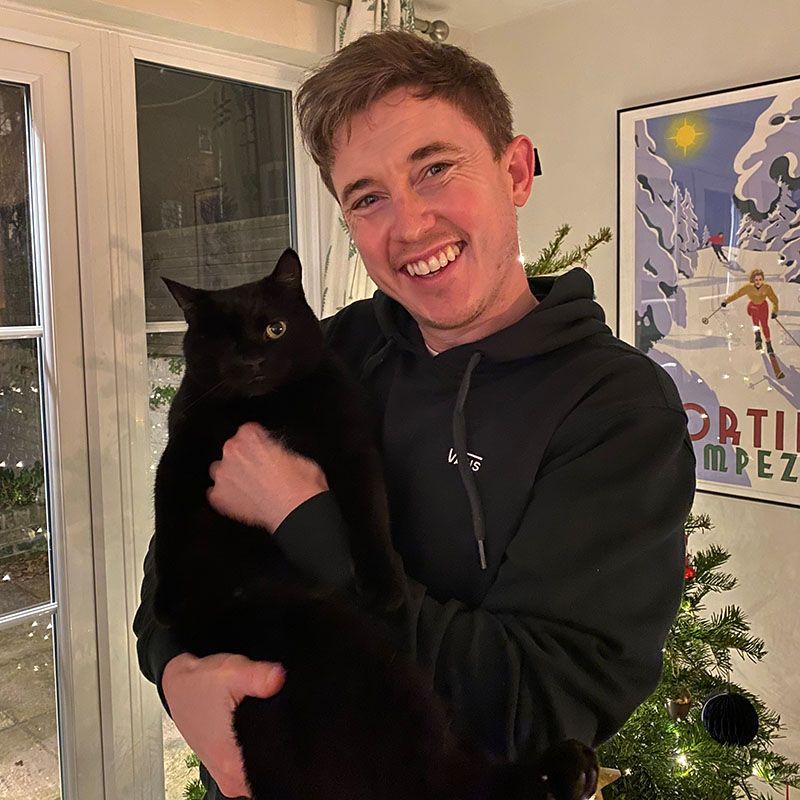 Jake Lambert is smiling and  holding his one-eyed black cat, Richard Parker