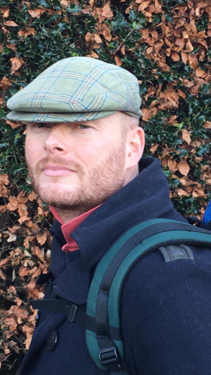 Jamie Thomson is wearing a green flat cap and a blue jacket. He has a beard and is looking directly into the camera.
