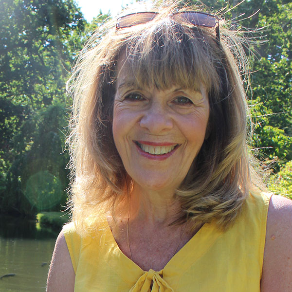 Kim Morley, epilepsy specialist midwife has long fair hair and is wearing a yellow dress with sunglasses on her head. She is smiling and looks relaxed