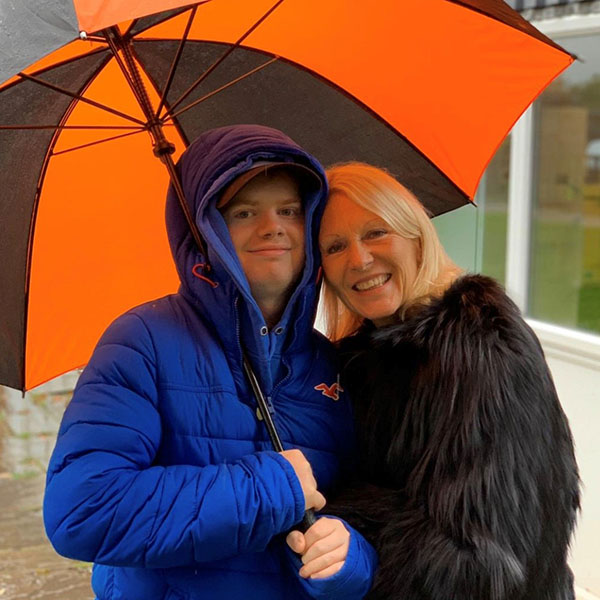 Muir Maxwell and his mum, Ann, sheltering under a bright orange and black striped umbrella