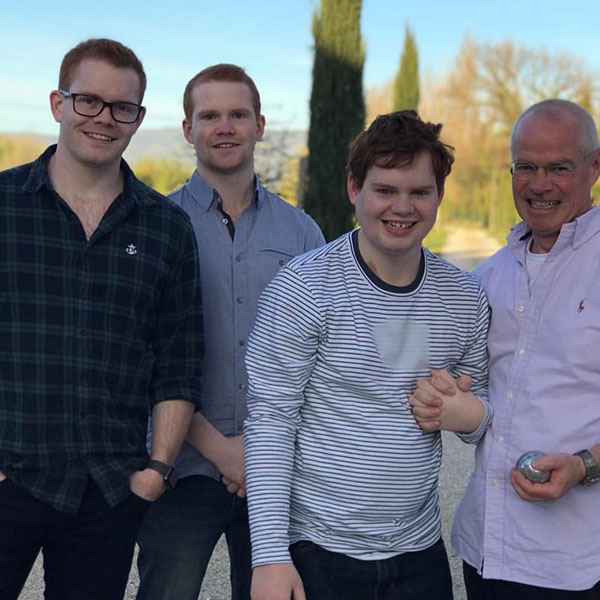 Muir in a family line up with his dad and two brothers. All are standing in a line and smiling happily. Muir's dad is holding his hand.