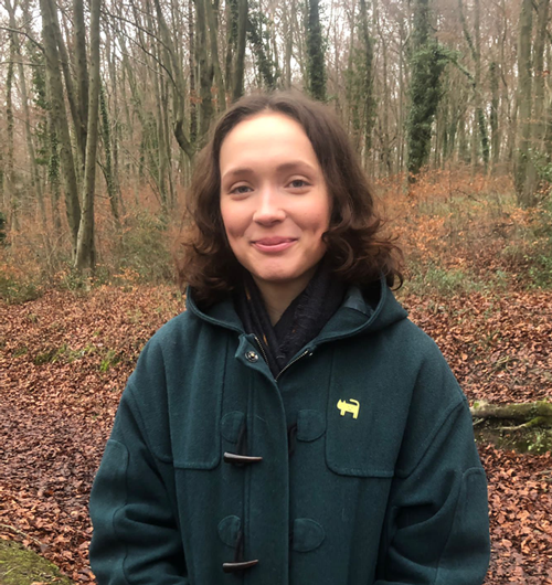 A head and shoulders picture of Paige Dawkins smiling and wearing a green coat, standing in the woods in Winter