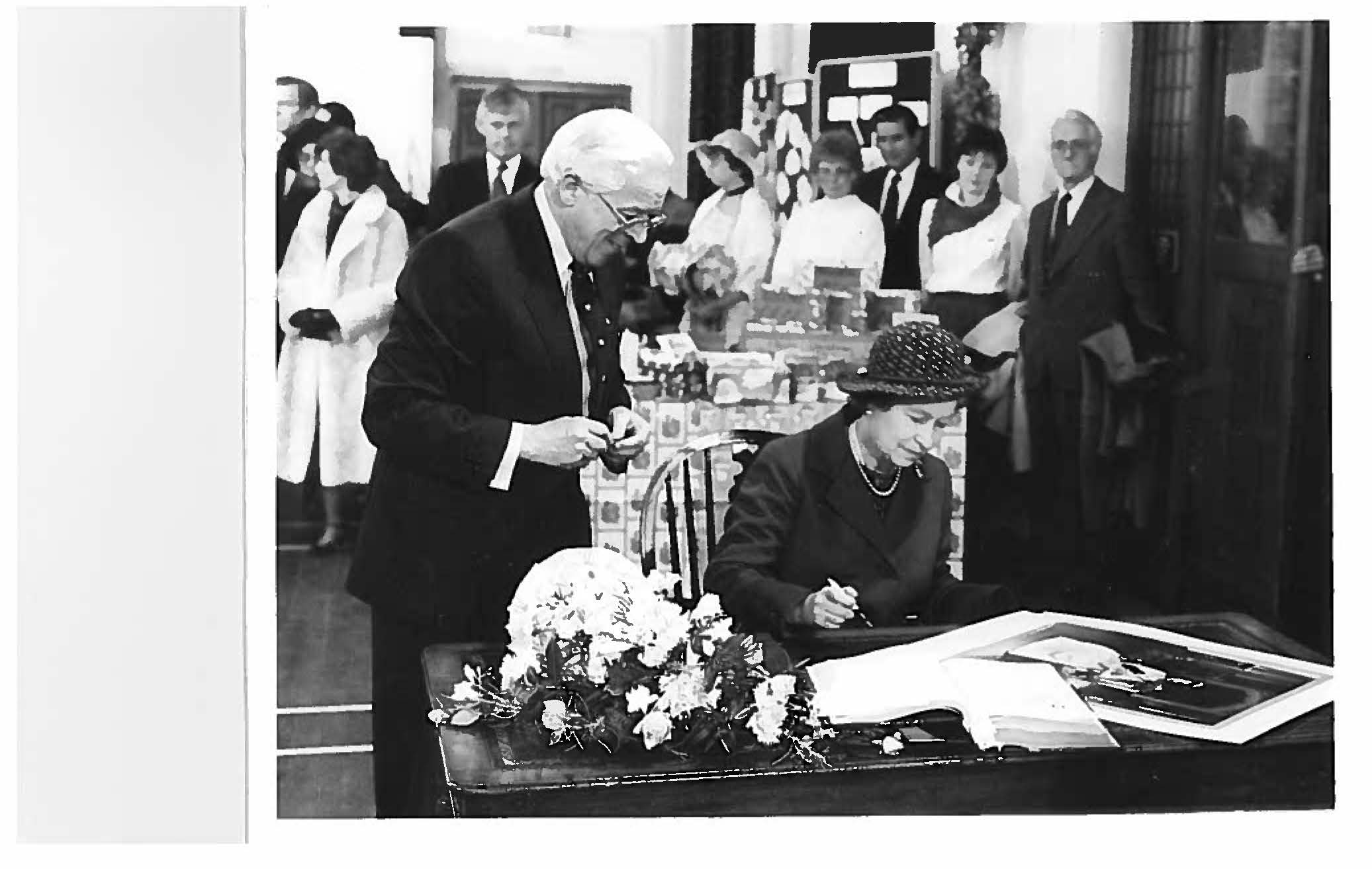 The Queen signs a book to commemorate her visit.