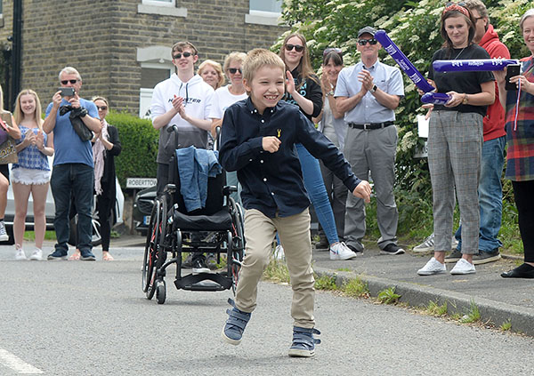 Zach Eagling completes his 2.6km challenge for Epilepsy Society. He is wearing smart trousers and a shirt and is cheered on by neighbours