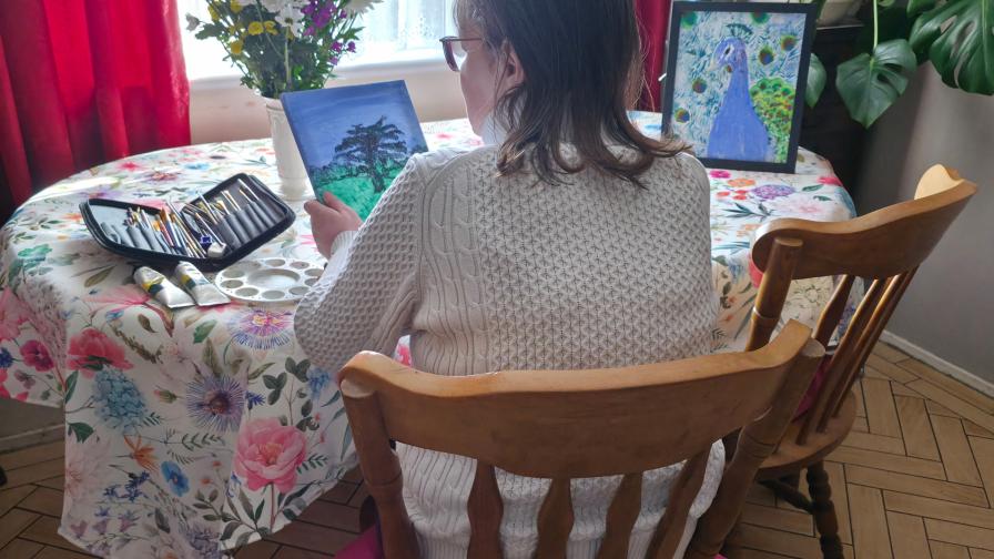 Woman with her back to the camera, painting at her dining room table