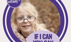 Little girl with blonde hair tied back and glasses smiling at the camera